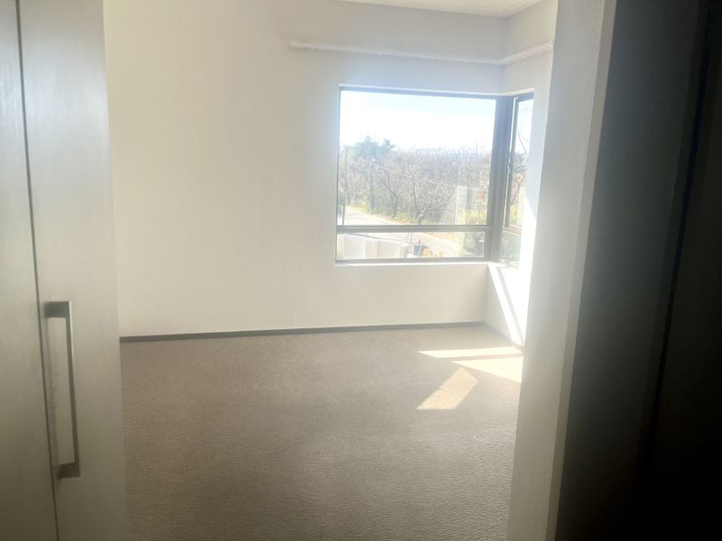 An empty bedroom featuring neutral carpeted flooring, a built-in cupboard, and a large corner window providing natural light.