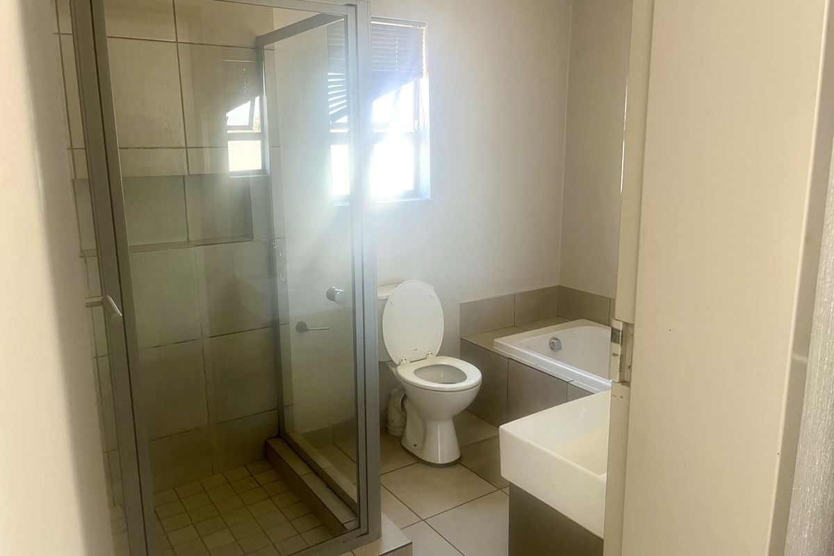 A functional bathroom featuring a glass-enclosed shower, a built-in bathtub, a toilet, and a vanity basin with neutral tiled finishes.