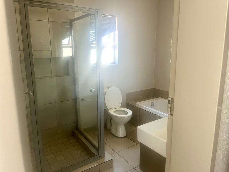 A functional bathroom featuring a glass-enclosed shower, a built-in bathtub, a toilet, and a vanity basin with neutral tiled finishes.