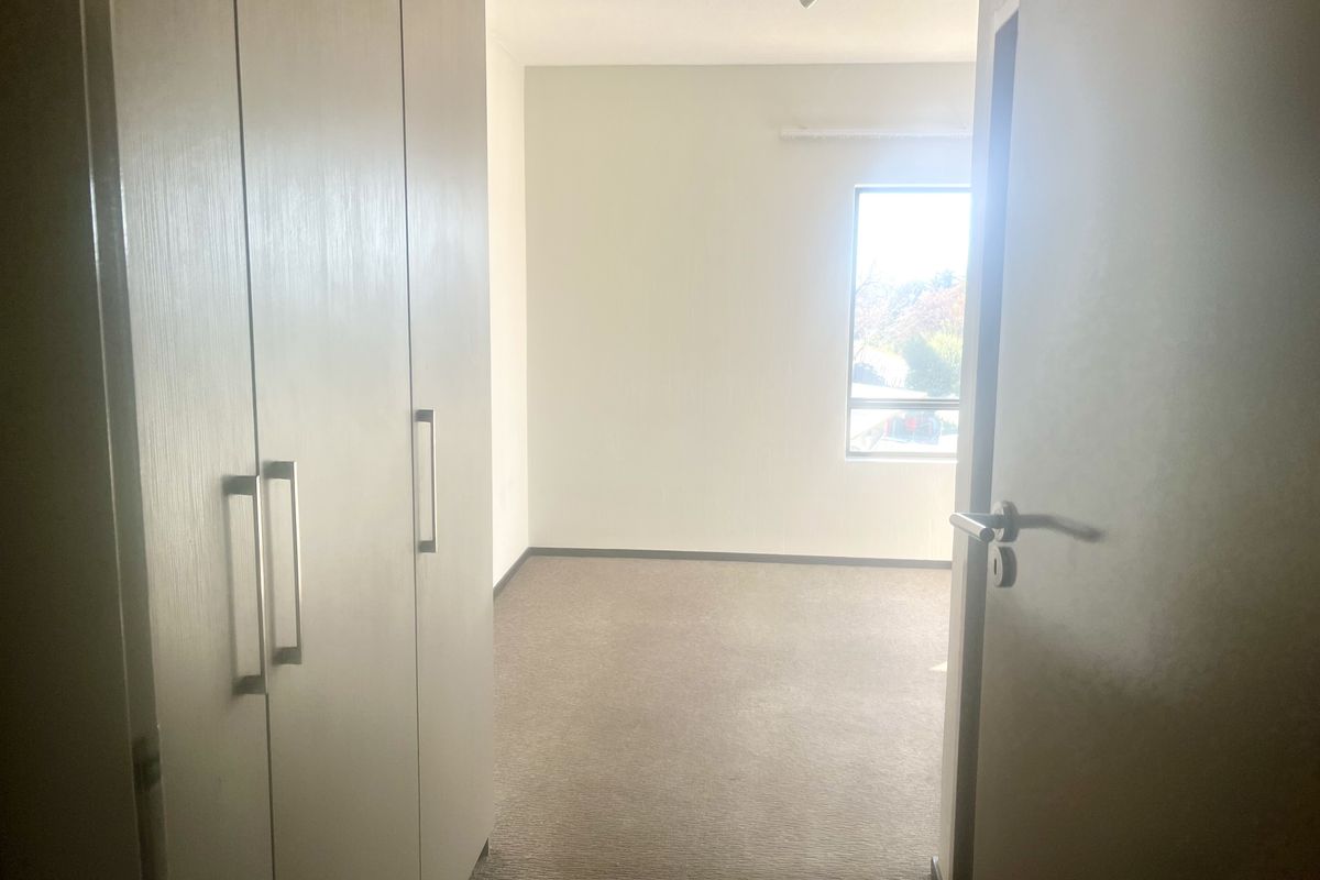 An empty bedroom featuring built-in cupboards, neutral carpeted flooring, and a window allowing natural light.