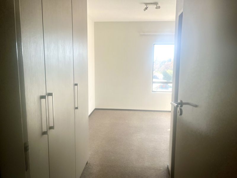 An empty bedroom featuring built-in cupboards, neutral carpeted flooring, and a window allowing natural light.