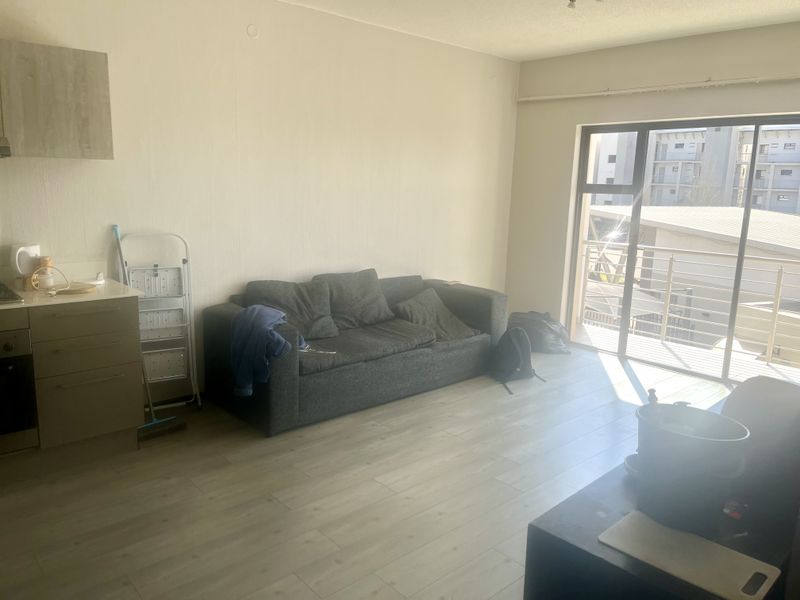 Open-plan living area featuring laminate flooring, a compact kitchen unit with built-in oven, and sliding door access to a balcony.