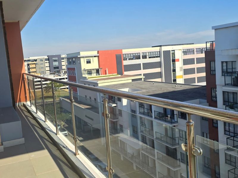 A balcony featuring a modern glass balustrade with a stainless steel handrail, offering an elevated view of the surrounding apartment complex.
