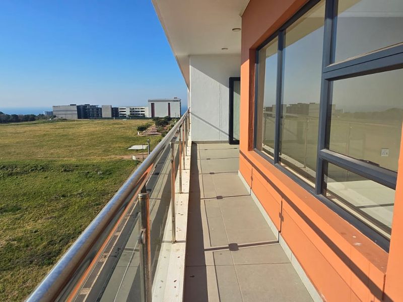 A spacious apartment balcony featuring a modern glass balustrade, tiled flooring, and expansive views over the surrounding landscape.