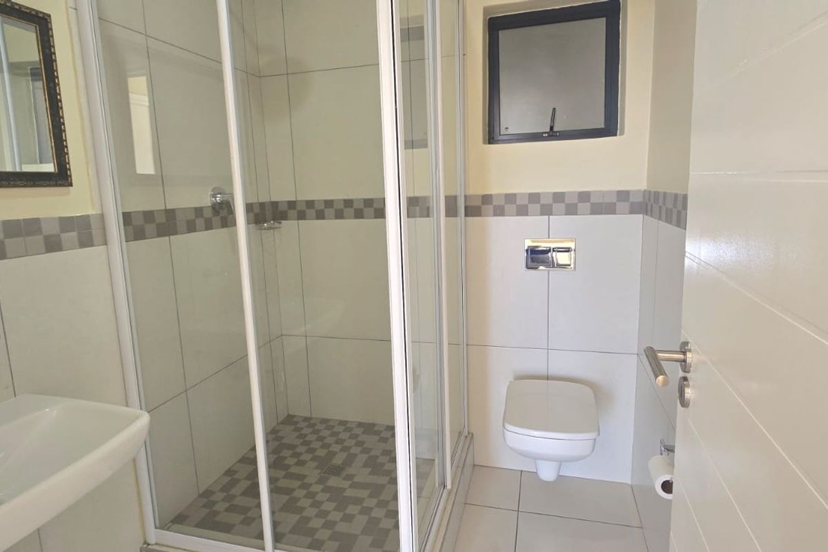 A clean, modern bathroom featuring a glass shower enclosure, wall-hung toilet, and pedestal basin with neutral tiling.