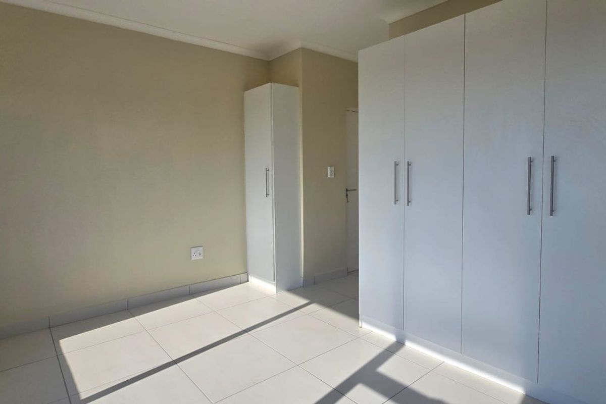 A bright, empty bedroom featuring neutral walls, white tiled flooring, and ample built-in cupboard storage.