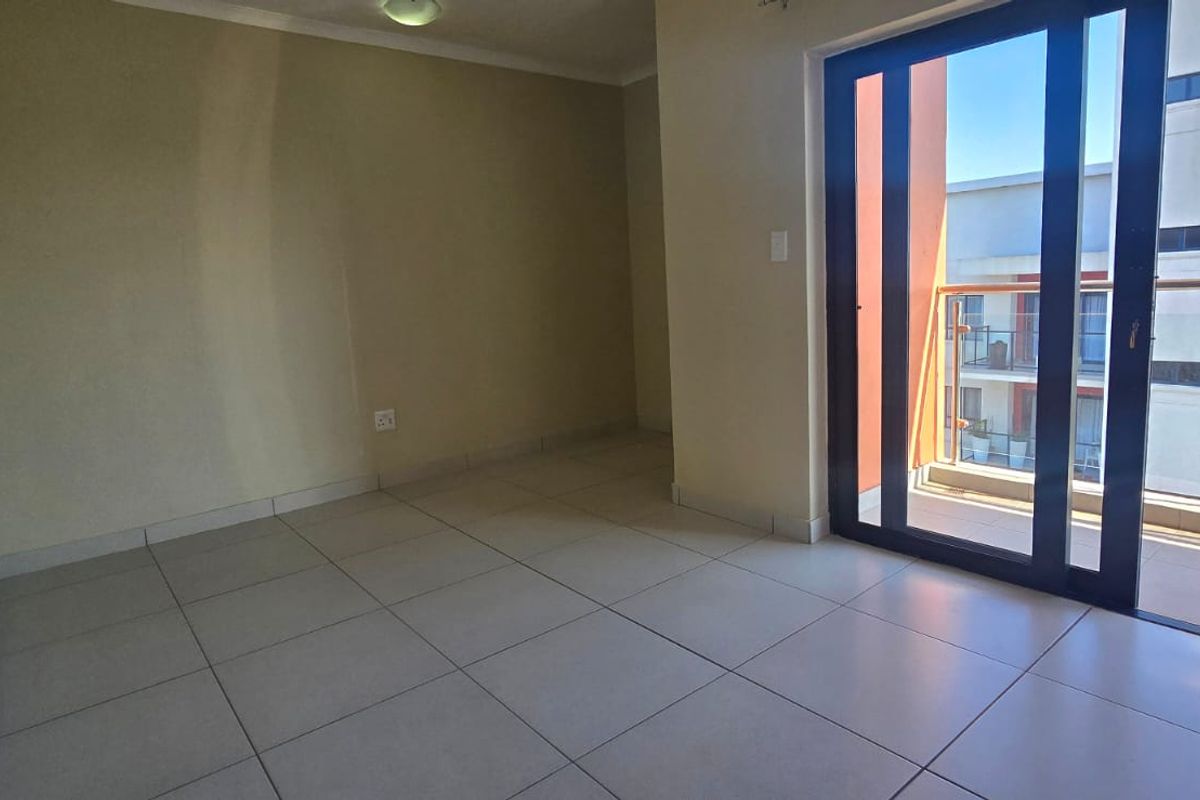 An empty, well-lit living area featuring neutral tiled flooring and a large sliding glass door providing direct access to a private balcony.