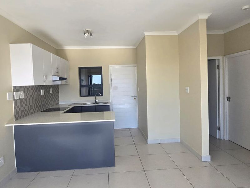 An open-plan kitchen area featuring modern cabinetry, stone countertops, integrated hob and extractor, and neutral tiled flooring in a clean, vacant space.