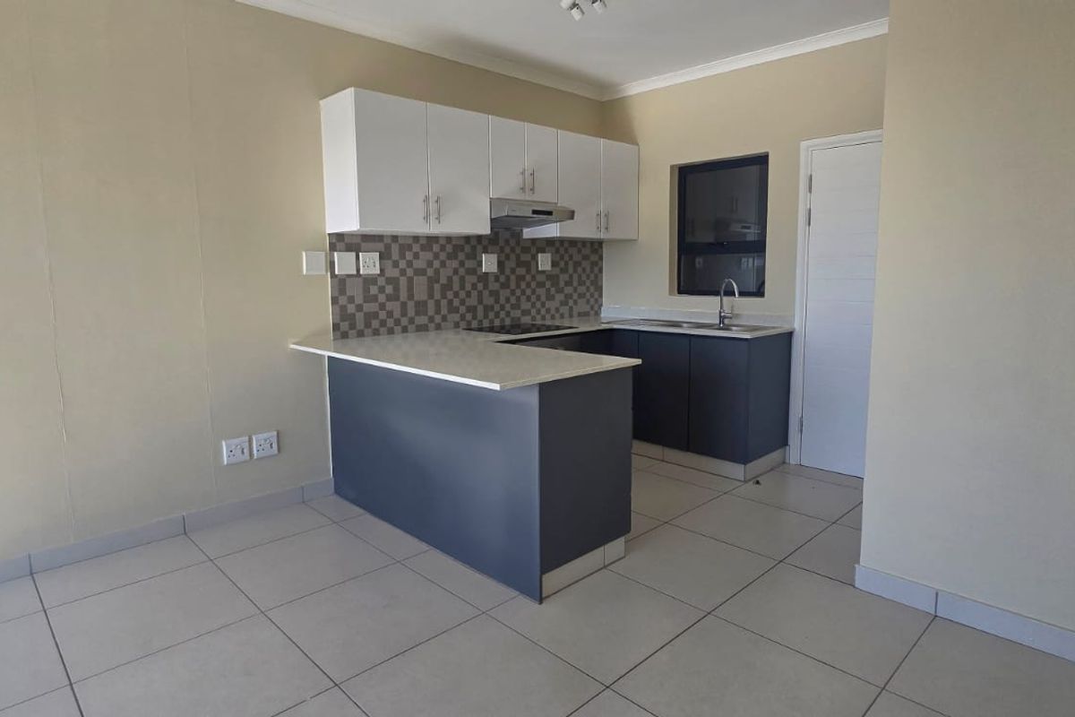 Modern kitchen featuring white upper cabinets, dark lower cabinetry, stone countertops, tiled backsplash, and integrated extractor fan with tiled flooring.