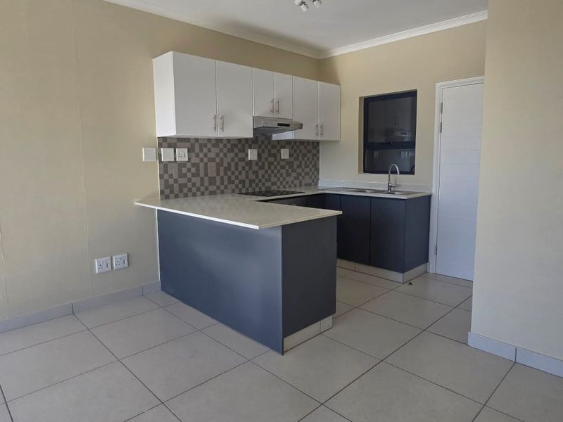 Modern kitchen featuring white upper cabinets, dark lower cabinetry, stone countertops, tiled backsplash, and integrated extractor fan with tiled flooring.