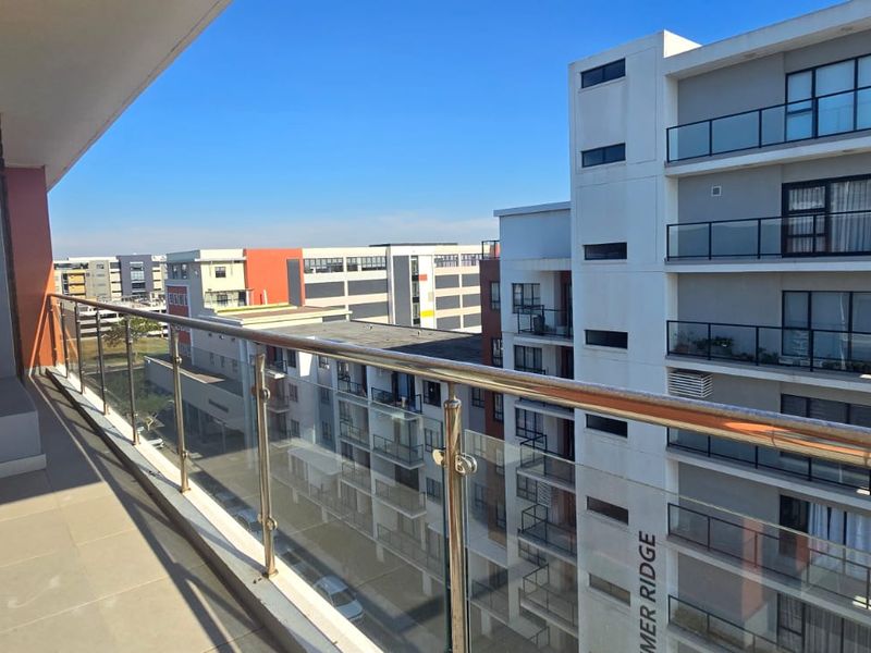 A spacious apartment balcony featuring a modern glass balustrade with stainless steel railings, offering an elevated view of the surrounding residential complex.