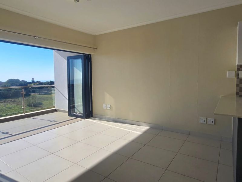 An open-plan living area featuring tiled floors, modern kitchen cabinetry with a mosaic backsplash, and large bi-fold doors opening onto a balcony with scenic views.