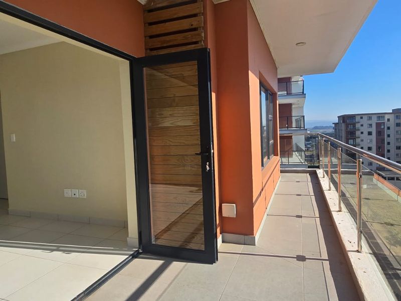 Spacious apartment balcony featuring a modern glass balustrade, tiled flooring, and seamless access to the interior living area.