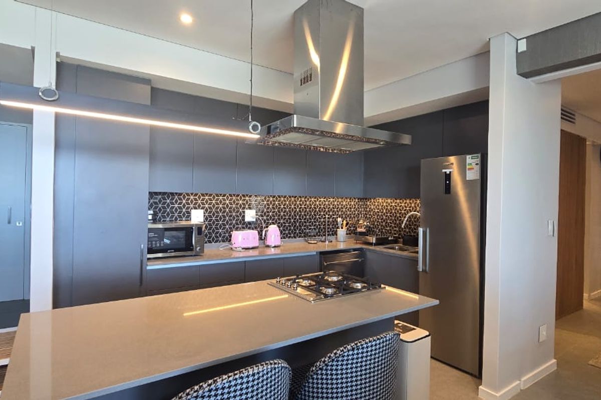 Modern kitchen featuring dark cabinetry, a stone island with a gas cooktop, stainless steel extractor fan, and a stylish geometric tile backsplash.