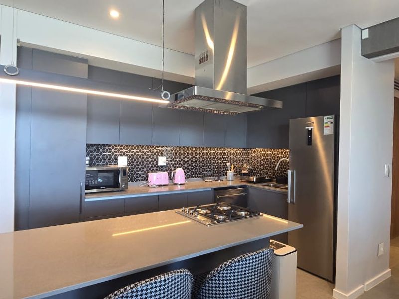 Modern kitchen featuring dark cabinetry, a stone island with a gas cooktop, stainless steel extractor fan, and a stylish geometric tile backsplash.