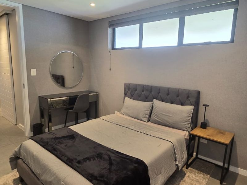 A modern, well-maintained bedroom featuring neutral grey tones, tiled flooring, recessed lighting, and a high-positioned clerestory window for natural light.