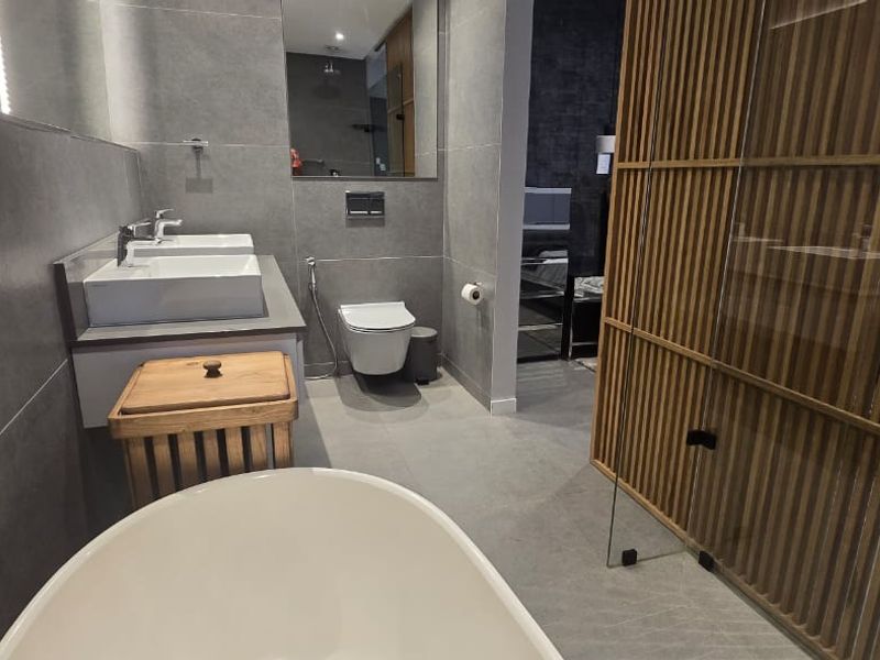 Modern bathroom featuring a double vanity, wall-hung toilet, and a freestanding bathtub, complemented by large format tiling and a decorative timber slat screen.