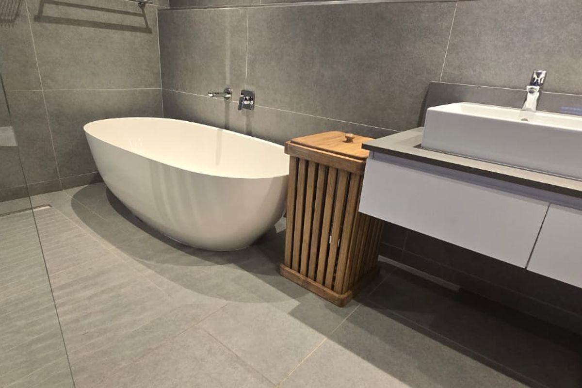 Modern bathroom featuring a sleek freestanding bathtub, glass-enclosed shower, and a contemporary floating vanity with a vessel sink and grey tiled finishes.