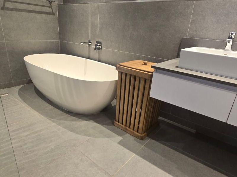 Modern bathroom featuring a sleek freestanding bathtub, glass-enclosed shower, and a contemporary floating vanity with a vessel sink and grey tiled finishes.