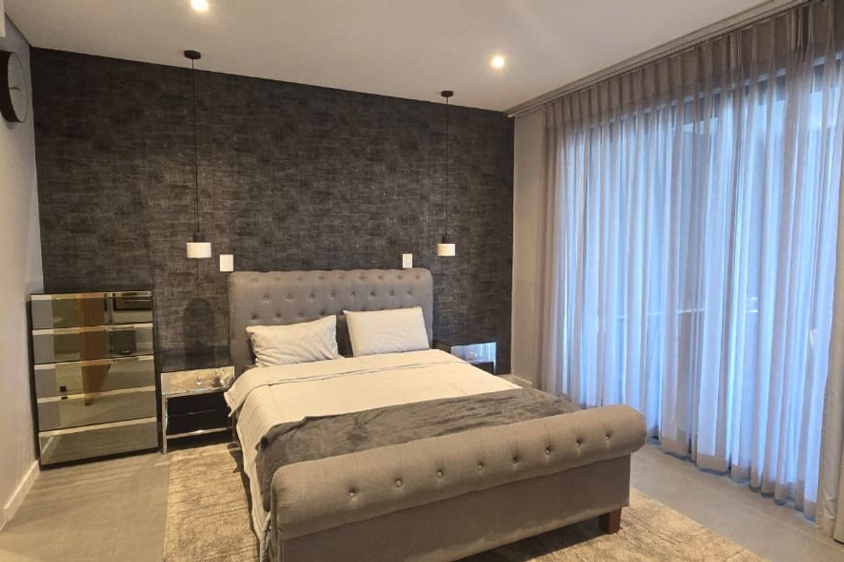 A modern, well-appointed bedroom featuring a textured feature wall, recessed lighting, floor-to-ceiling curtains, and neutral tiled flooring.