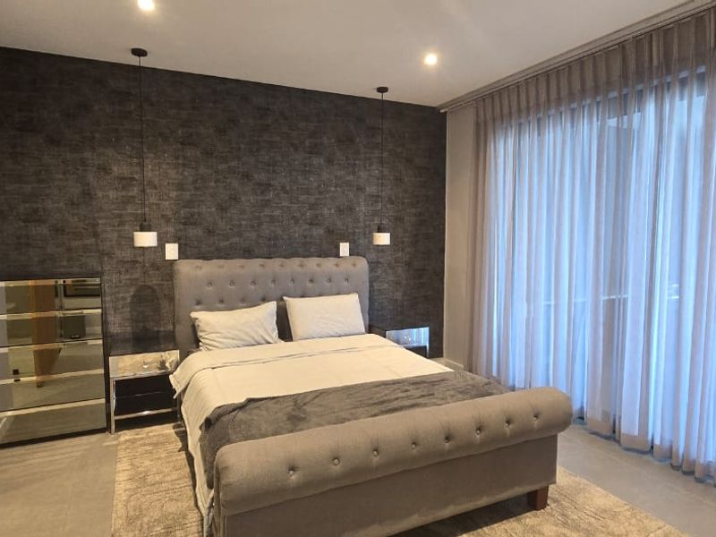 A modern, well-appointed bedroom featuring a textured feature wall, recessed lighting, floor-to-ceiling curtains, and neutral tiled flooring.