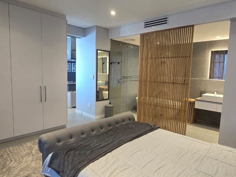 Modern bedroom featuring extensive built-in cabinetry and an open-plan en-suite bathroom with a stylish timber privacy screen and contemporary fixtures.