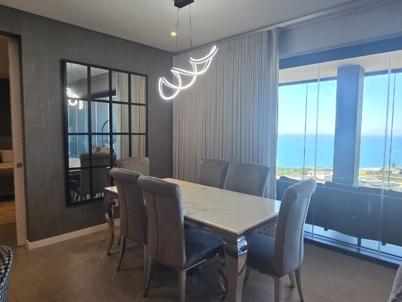 Modern dining area featuring contemporary lighting, a feature wall, and floor-to-ceiling glass sliding doors offering expansive ocean views.