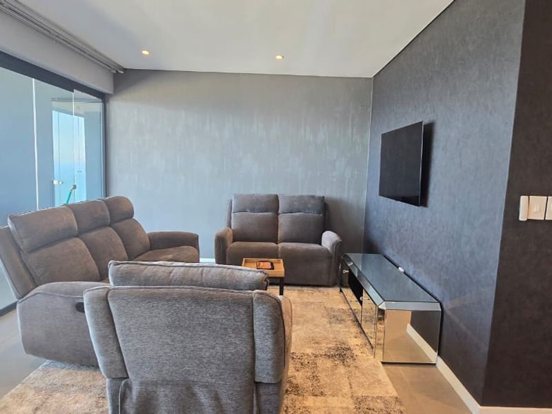 Modern living room featuring a textured feature wall, recessed downlighting, and large sliding glass doors leading to an outdoor balcony area.