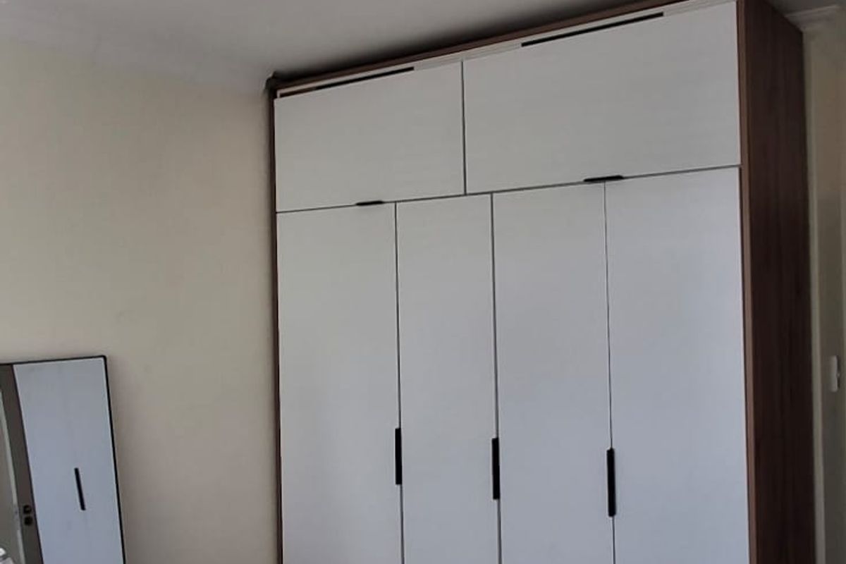 A bedroom featuring a modern, full-height built-in wardrobe with white doors and dark handles.