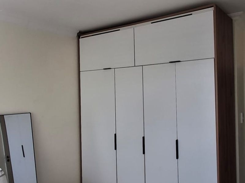 A bedroom featuring a modern, full-height built-in wardrobe with white doors and dark handles.