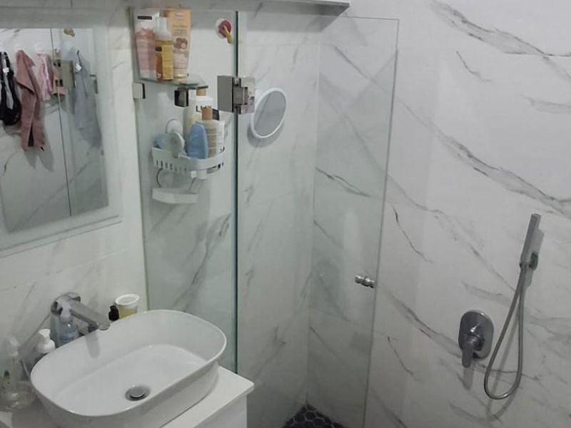 Modern bathroom featuring marble-look wall tiles, a walk-in shower with rain head, black hexagonal floor tiling, and a sleek white vanity with vessel sink.