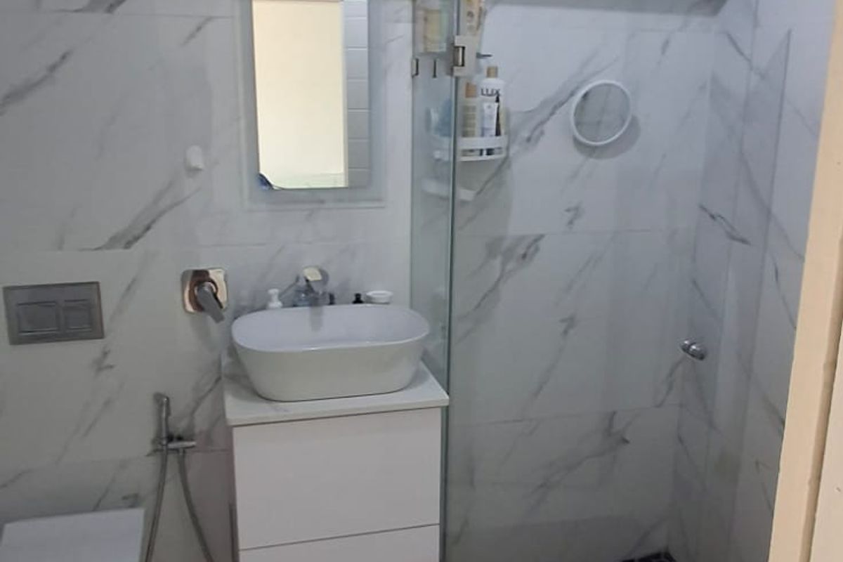Modern bathroom featuring marble-look wall tiles, a wall-mounted toilet with concealed cistern, vanity basin, and a glass-enclosed shower with a rainfall shower head.