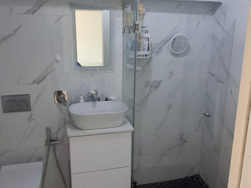 Modern bathroom featuring marble-look wall tiles, a wall-mounted toilet with concealed cistern, vanity basin, and a glass-enclosed shower with a rainfall shower head.