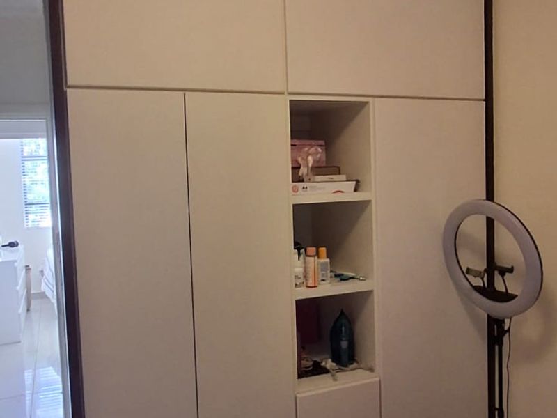 A bedroom featuring a large, modern built-in wardrobe with integrated shelving and clean white finishes, complemented by tiled flooring.
