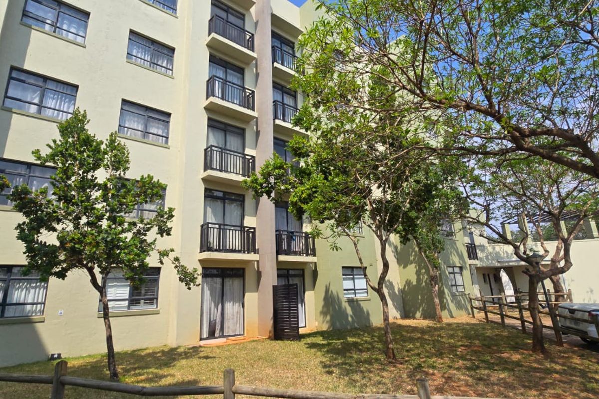 Exterior view of a multi-story apartment building featuring private balconies, sliding glass doors, and landscaped grounds with mature trees.