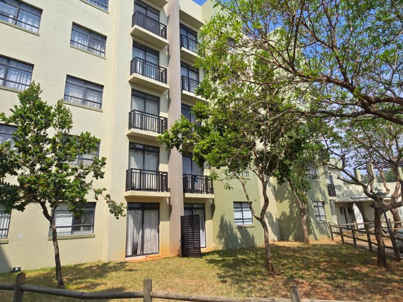 Exterior view of a multi-story apartment building featuring private balconies, sliding glass doors, and landscaped grounds with mature trees.