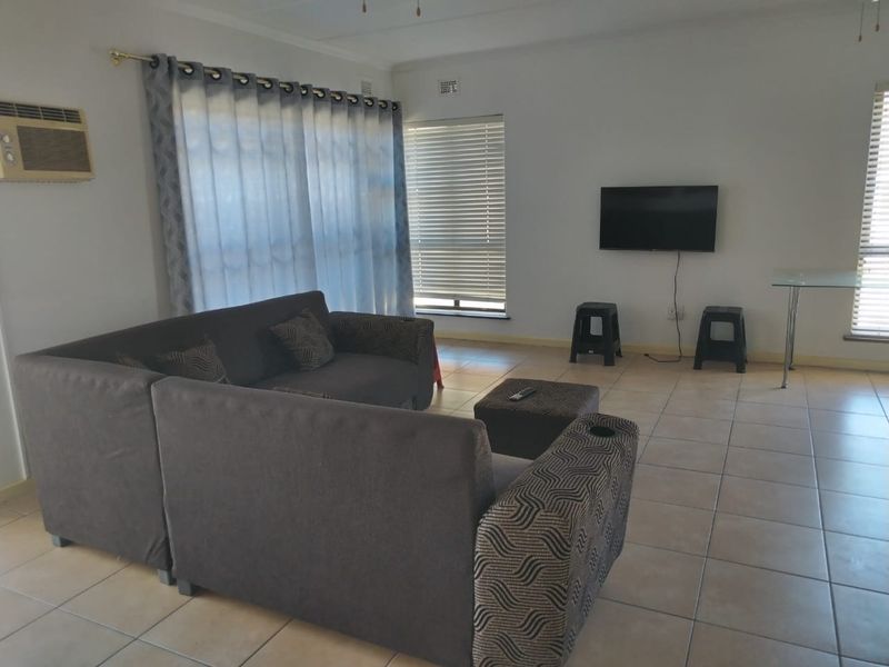 A spacious living area featuring neutral ceramic floor tiles, window blinds, and a wall-mounted air conditioning unit.