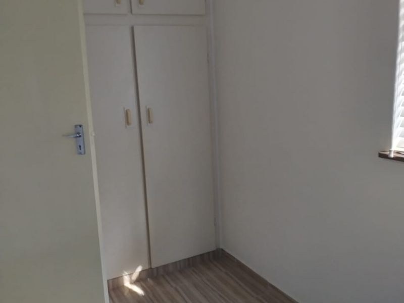 A bedroom featuring built-in cupboards, tiled flooring, and a window with blinds, offering a clean and functional space.