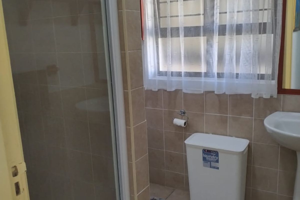 A functional bathroom featuring a shower enclosure, pedestal basin, and neutral wall and floor tiling.
