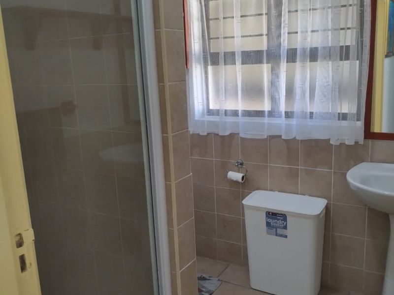 A functional bathroom featuring a shower enclosure, pedestal basin, and neutral wall and floor tiling.