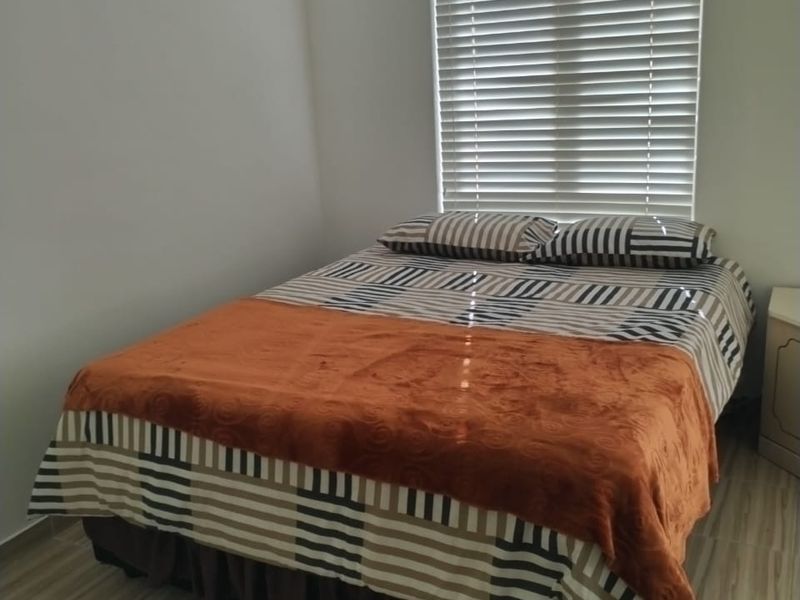 A simple bedroom featuring tiled flooring and a window fitted with venetian blinds.
