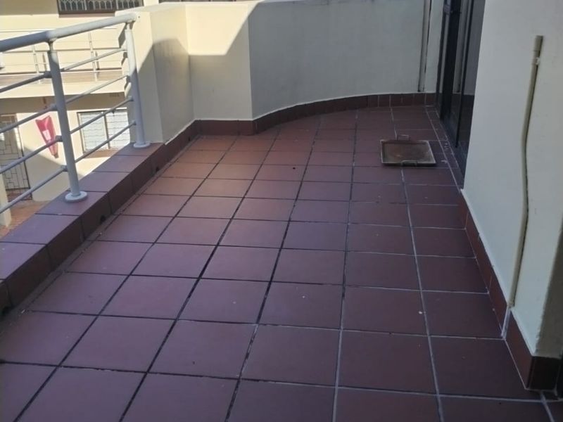 A spacious apartment balcony featuring tiled flooring and a metal balustrade, offering an open outdoor area accessible via a sliding door.