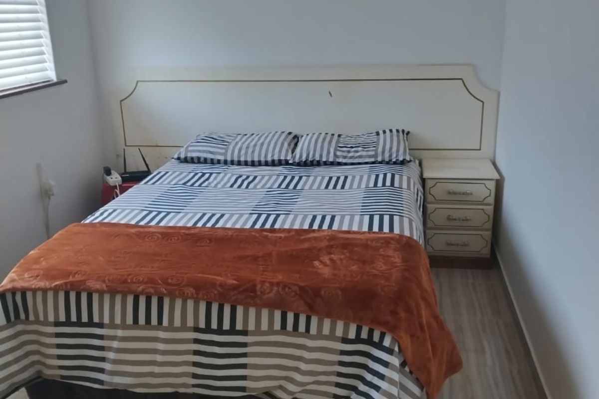 A functional bedroom featuring tiled flooring, a built-in headboard, and venetian blinds, offering a clean and simple living space.
