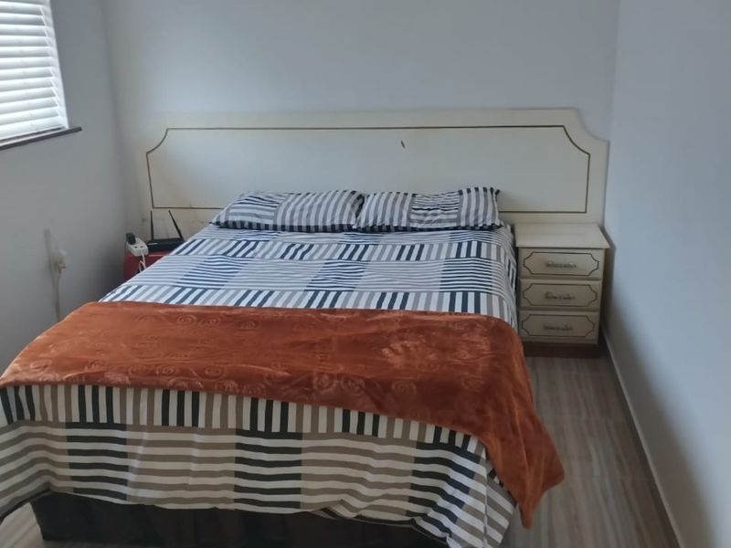 A functional bedroom featuring tiled flooring, a built-in headboard, and venetian blinds, offering a clean and simple living space.