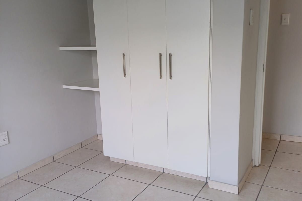 A clean, empty bedroom featuring neutral tiled flooring and a white built-in wardrobe with integrated shelving.