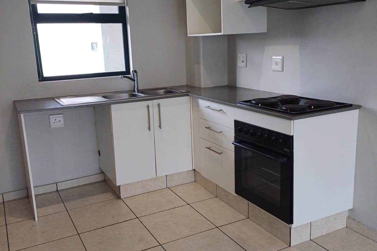 A clean, functional kitchen featuring white built-in cabinetry, a stainless steel sink, an electric stove with an oven, and tiled flooring.