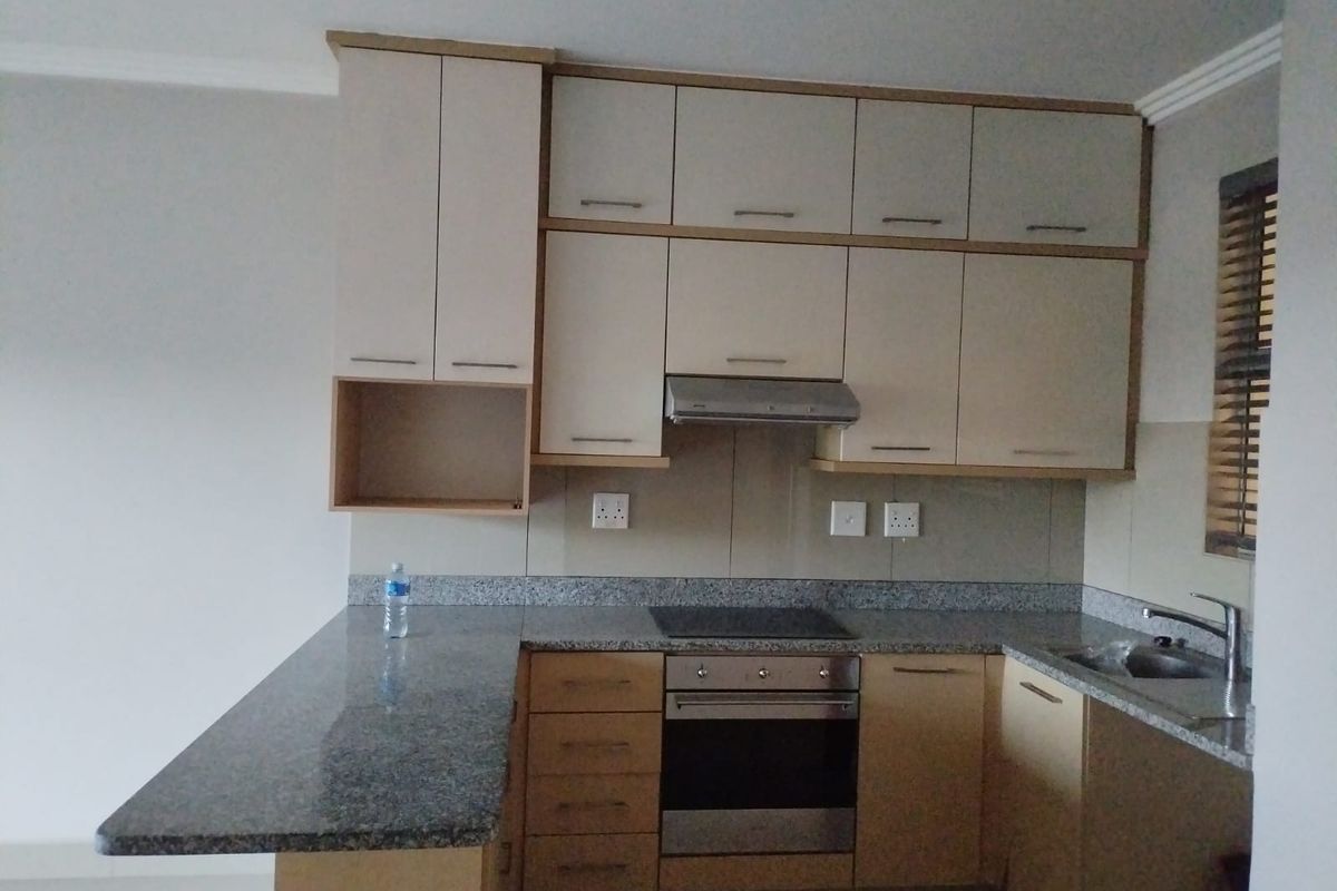 A functional kitchen featuring granite countertops, built-in cabinetry, an integrated oven, electric hob, and a stainless steel sink with a tiled backsplash.