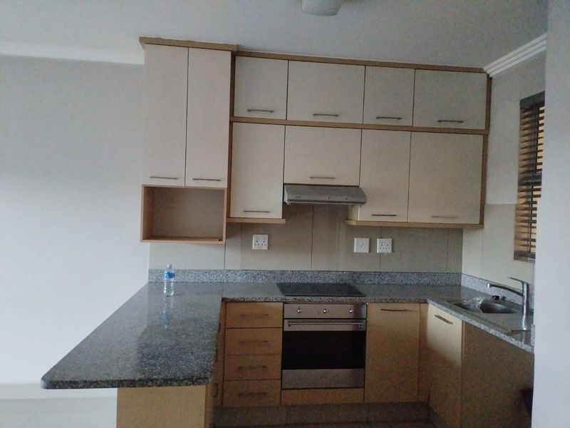 A functional kitchen featuring granite countertops, built-in cabinetry, an integrated oven, electric hob, and a stainless steel sink with a tiled backsplash.