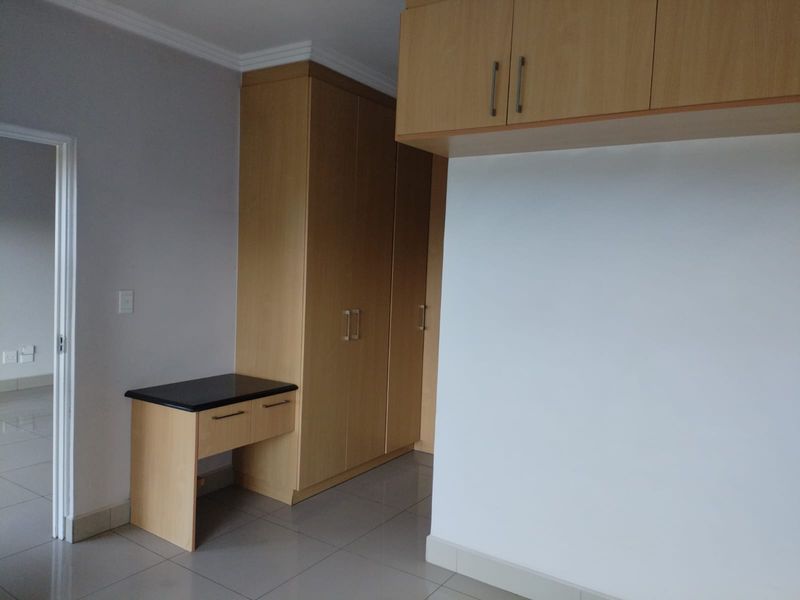 A clean, empty bedroom featuring light wood built-in cupboards, a matching vanity unit with a dark countertop, and neutral tiled flooring.