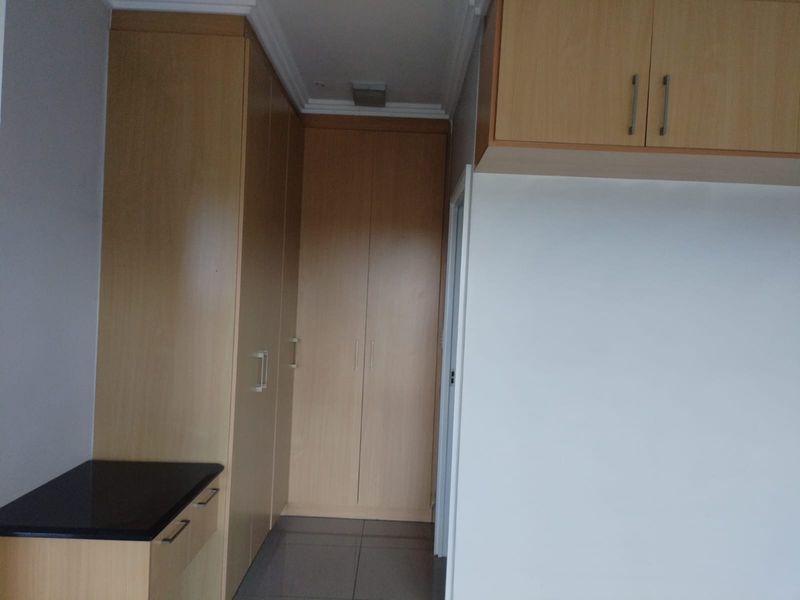 A bedroom featuring extensive built-in wooden cabinetry, overhead storage, a vanity unit with a dark countertop, and tiled flooring.